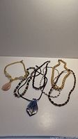 Lot of six necklaces on white surface. Includes pearl, stone bead and Monet vintage styles.