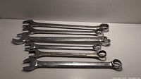 Eight oversized combination wrenches laid out on a flat surface, showing both open-end and ring-end sides, chrome finish visible.