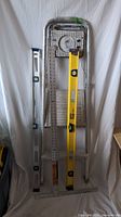 Full view of lot with two spirit levels, T-square, metal ruler and other measuring tool against white backdrop.