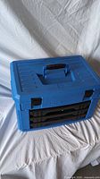 Closed blue Mastercraft toolbox with black handle and latches on white fabric background