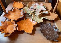 Top view of all 10 ceramic leaf dishes arranged on wooden surface, showing a variety of colors and sizes representing fall leaves.