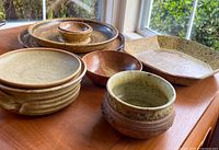 Top view of most ceramic pieces including brown, beige, and rust toned bowls and plates arranged on a wooden surface near a window.