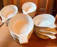 Top and angled view of stacks of white ceramic soup bowls showing their round shape and handles.