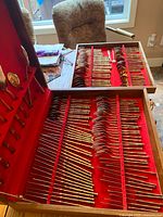 View of the lower layer of the wooden box with rows of bronze flatware pieces including forks and spoons with bamboo-style handles.