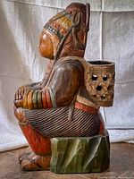 Side profile view showing detailed painted headdress, clothing, and basket on back with hexagonal cut outs.