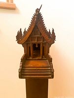 Close-up front view of the Thai spirit house showing detailed wood carvings and entrance platform.