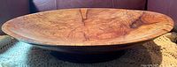Side view of the turned wooden platter showing its oval shape, smooth finish, and natural wood grain textures.