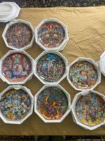 Top view of 8 Franklin Mint cat themed plates shown in plastic display holders on a beige cloth surface.