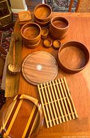 Collection of wooden kitchenware on a wooden table showing multiple bowls of various sizes, coasters, trivets, wooden spoon, and spoon rest.