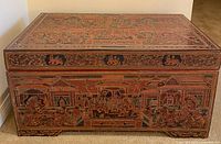 Front of first lacquerware chest showing painted traditional scenes in black, red, and gold