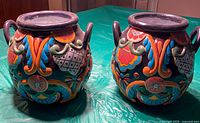 Pair of Mexican ceramic jars with colorful floral and geometric raised relief patterns, viewed from the front and side, showing their shape and design details.