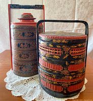 Image showing front view of the two stacked food carriers with lids and carrying handles, highlighting intricate painted decorative patterns.