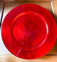 Single red round charger plate, 12 inches diameter, showing its metallic finish and slight wear.