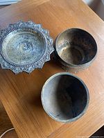 Top view showing three metal items: a decorative bowl with ornate edges, a rounded bowl, and a smaller bowl with figures inside.