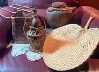 Photo of four assorted items including a rattan basket, wooden storage container with woven lid, traditional oil carrier in wicker case, and a large wicker fan, displayed on a red couch.