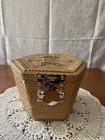 Hexagonal wicker basket case with a metal latch for securing the lid, photographed closed on a lace doily.