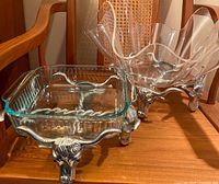 Two glass serving dishes on detailed Longhorn cattle metal stands, showing full view of both dishes and stands side by side on wooden chair.