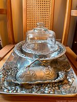 Photo of serving pieces including cake pedestal with glass dome, butter dish with pewter cover, and serving platter.