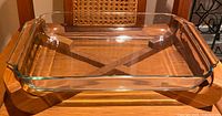 Clear rectangular Pyrex style glass baking dish on wooden trivet on chair