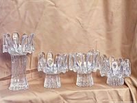 Four clear glass tea light holders of varying heights with textured bases and wavy, artistic rims arranged in a row against a beige backdrop.