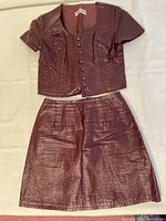 Front view of 1960s burgundy faux leather miniskirt set, showing top with metal buttons and matching miniskirt.