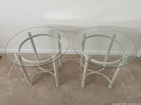 Top-front view of the two contemporary round glass top end tables side by side, showing clear glass tops and cream-colored bases with circular structural supports.