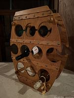 Front and side view of barrel-shaped wooden wine rack holding two wine bottles showing natural wood finish and metal rivets