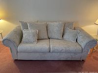 Frontal view showing sofa with six cushions and floral textured beige fabric upholstery.