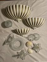 Overview photo of all decor items arranged on fabric including three shell-inspired white and gold wall sconces, several textured and fluted glass bowls, two shell-shaped soaps, and two starfish glass candleholders.