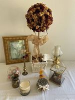 Full view of the collection on table including dried rose topiary with ribbon, framed picture, brass holder, glass cube and candles.