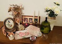 Wide shot showing entire curated collection including green glass vessel, photo frame, candlesticks, floral arrangements, satin lace bag, tray, and paperweight.