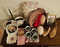 Full collection displayed on wooden surface including mugs, textiles, hat, basket, framed print, candy dish, shoe forms.