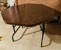 Full view of the octagonal poker table showing the woodgrain pattern surface and folding black metal legs.