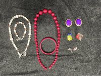 Lot contents include vintage necklaces, bracelet, earrings, and pins arranged on black background.