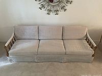 Front view of cream upholstered three-seat sofa with wood arm details and fabric skirt.