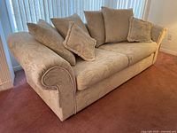 Side angle of one cream fabric sofa showing rolled arm and cushions.