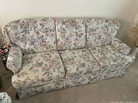 Front view of the three-seat floral patterned sofa showing floral fabric upholstery, padded armrests, and three seat cushions.