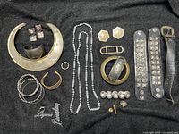 Overview of the vintage heavy metal jewelry set spread out on black cloth showing cuff necklace, metal rings, bracelets, earrings, belt and pins.