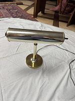 Photo of brass banker's lamp standing on surface showing off the cylindrical shade and round base with power cord.