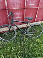 Side view of green Raleigh Matterhorn mountain bike showing frame, tires, saddle and handlebar against a red fence.