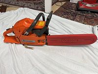 Side view of chainsaw showing orange housing, black wrap handle and red bar cover