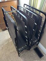 Photo of two black folding cots standing side by side, showing the fabric resting area and metal frames.