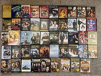 Photo shows a collection of 40 DVD cases arranged in rows, featuring titles such as John Wayne collections, Bonanza TV show series, James Bond movies, Sherlock Holmes, classic westerns, comedy films, and holiday specials.