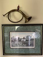 Photo showing brass bugle mounted above the framed print with a hunting scene.