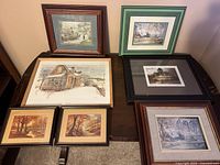 Photo of seven framed prints including a rustic winter building, autumn landscapes, and urban scenes.