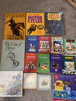 Photo displaying a collection of children's books including The Big Book of Cowboys, All About Motor Cycles, Great Trains, The Love of Horses, multiple Noddy books, Mother Goose, and My Pets sound book.