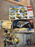 Overview of the two original LEGO sets boxes and assorted loose LEGO pieces in yellow, black, blue, and grey on carpet.