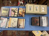 Top view of multiple photo albums with various cover designs and two decorative boxes on a blue cloth.