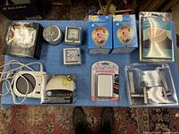 Overview of various household and decorative items laid out on blue cloth including nightlights, kitchen timer, decorative spheres, cube shakers, and ceramic coffee collar.