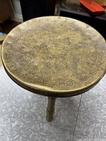 Top view of round brass stool showing intricate floral and geometric engravings on the seat surface.